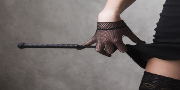 A hand wearing a mesh glove, holding a riding crop next to a thigh